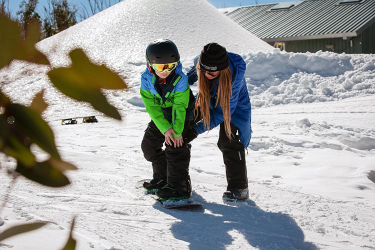 a kid learning to go down the hill on a snowboard with an instructor by his side