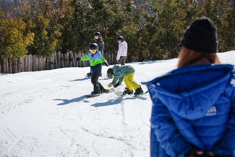 a group of kids riding down the hill on a snowboard