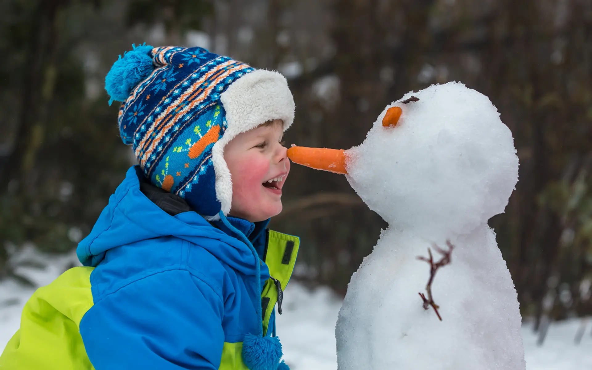 boy smiling and touching nose with a snowman