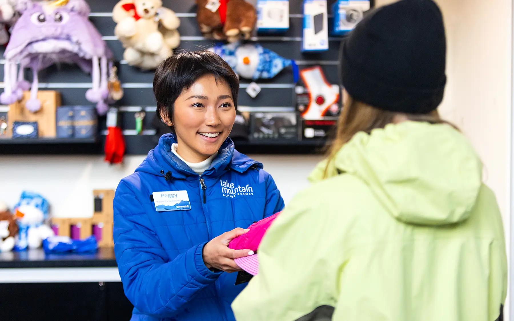 Employee hands an item to customer, with shelves of plush toys in the background.